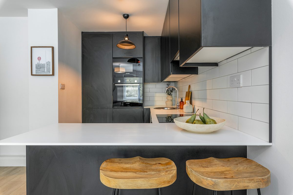 White breakfast bar with wooden stools, integrated oven and extractor in EirStay Islandbridge serviced apartment kitchen Dublin 8