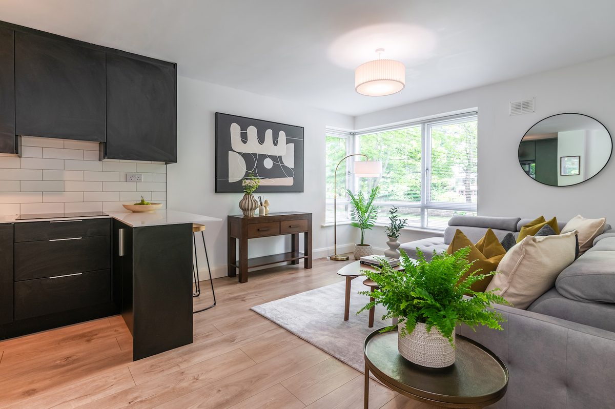 Open-plan living and kitchen area in EirStay Islandbridge serviced apartment Dublin 8 — matte-black fitted kitchen with breakfast bar and bright corner-sofa lounge