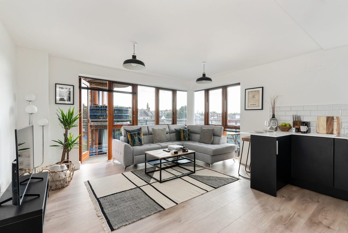 Open plan living room with grey L-shaped sofa balcony doors and industrial pendants in EirStay serviced apartment Kilmainham Dublin 8